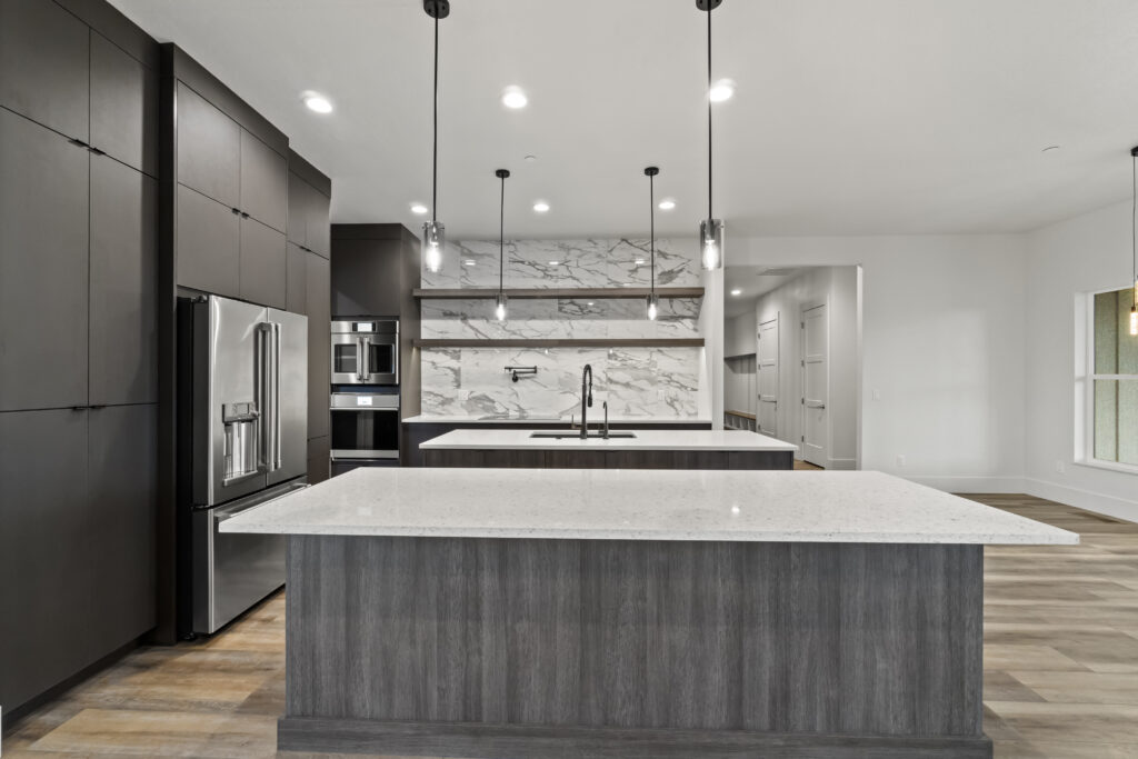 Kitchen in The Ascent floor plan with double islands, dark cabinetry, marble-look backsplash, pendant lighting, and open shelving.
