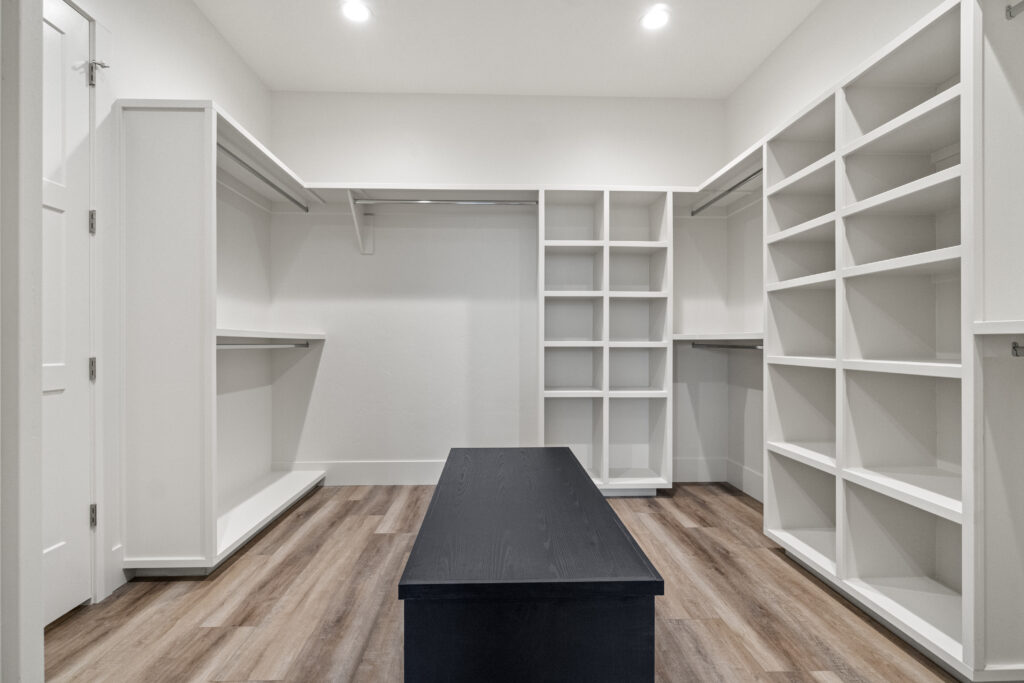 Custom primary closet in The Ascent floor plan with built-in shelving, hanging storage, wood-look flooring, and center island.